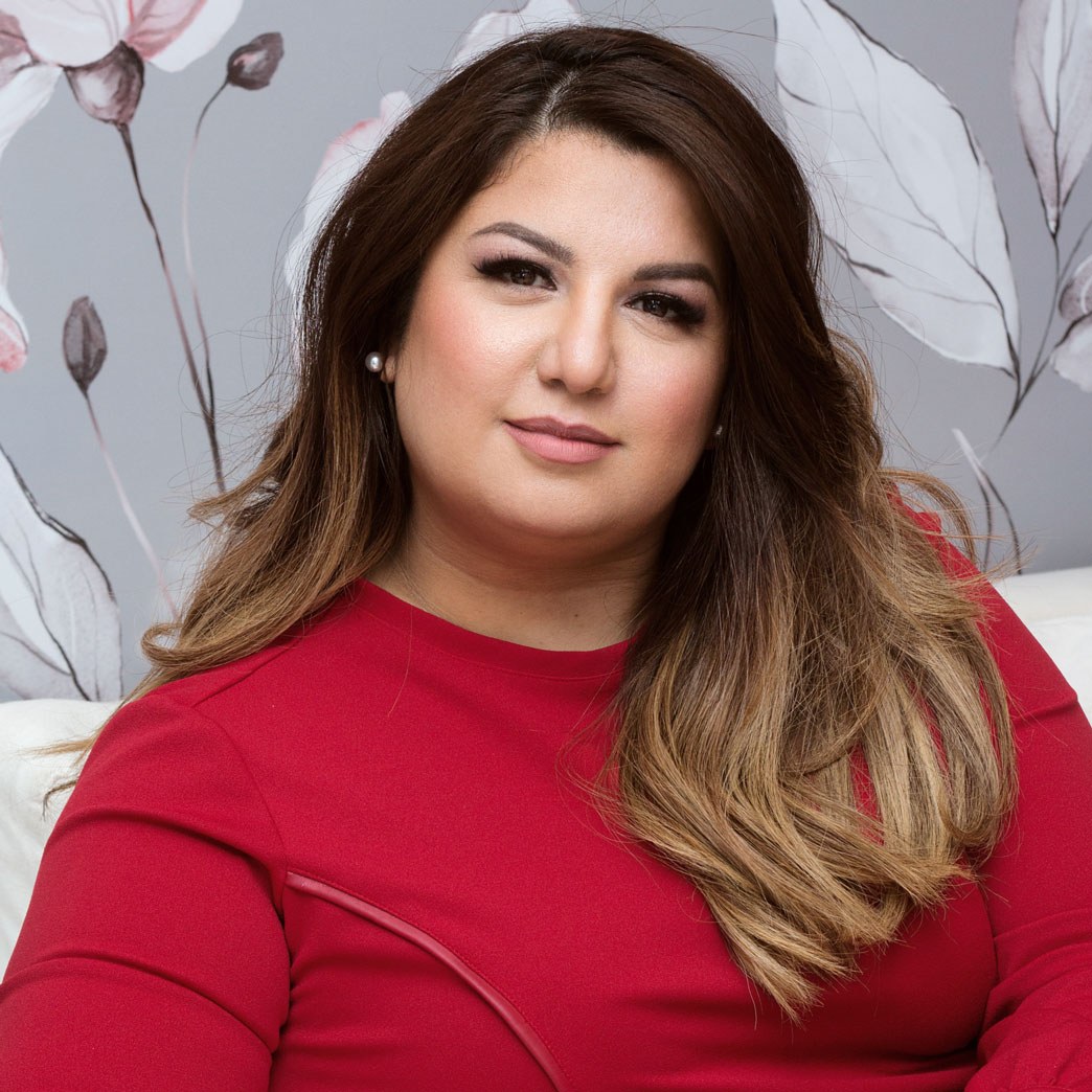 Retrato de Daiana, CEO de DR Estética, luciendo un elegante vestido rojo. Está sentada frente a un fondo floral suave, transmitiendo profesionalismo y confianza.